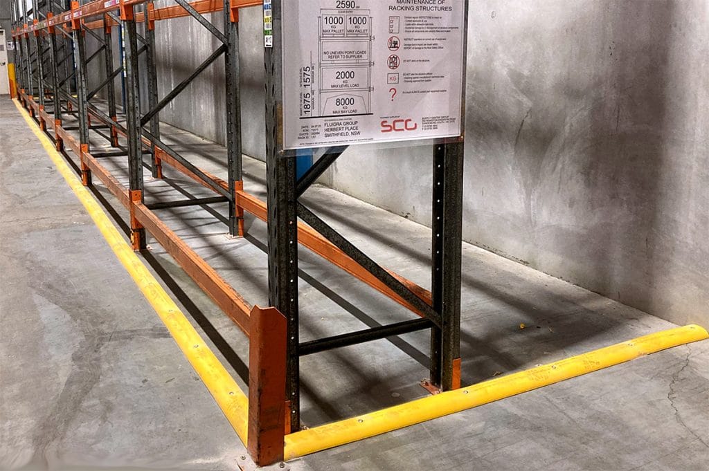 Heavy-duty yellow rubber floor bunding installed in a warehouse to contain spills and protect shelving areas