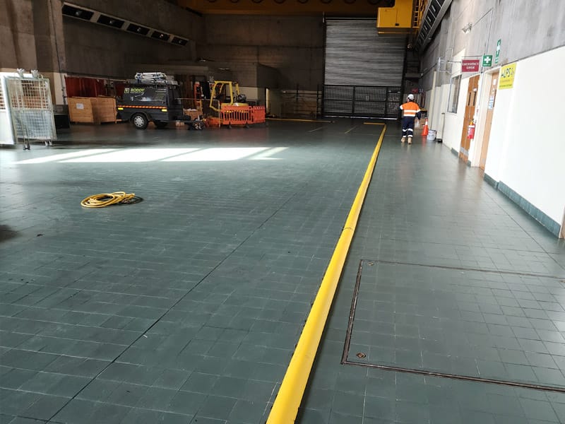 Yellow rubber floor bunding installed along the edge of a tiled warehouse floor for spill containment and vehicle guidance.