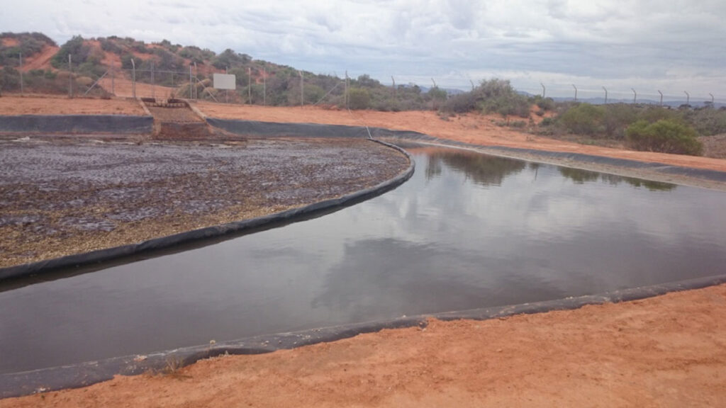 Heavy duty XR5 containment boom isolating surface oil and grease layer in industrial waste pond.