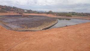 XR5 heavy duty containment boom installed in industrial waste transfer pond separating oil layer from water.