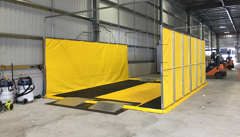 Portable wash bay with bunded containment mat and spray curtains installed inside an industrial facility